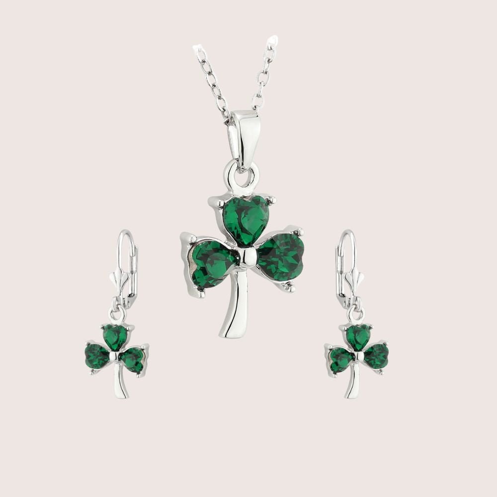 Silver jewelry set with green gemstones on a light pink background